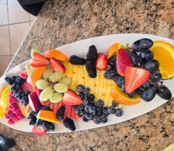 A platter of assorted fresh fruits including pineapple, strawberries, grapes, orange slices, raspberries, and blackberries.