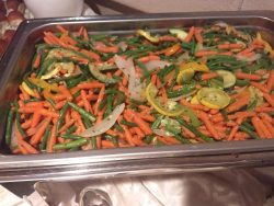 A stainless steel tray filled with steamed carrots, green beans, onions, and yellow squash.