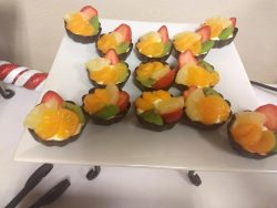 Chocolate cups filled with sliced strawberries, kiwi, pineapple, and mandarin oranges arranged on a white plate.