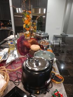 A kitchen island displays a soup pot, crockpots, a pumpkin, and a tall vase with decorative gourds and branches.