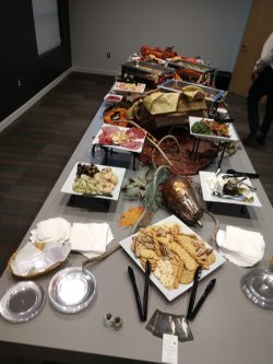 A table set with assorted appetizers, crackers, fruit, meats, and cheese, ready for self-service at an event.