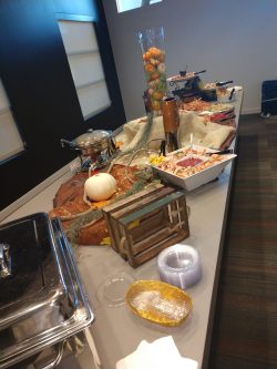 Buffet table with assorted dishes, serving utensils, plates, plastic bowls, and autumn-themed decorations.