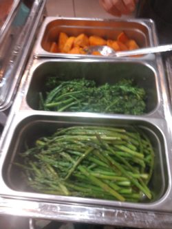 Three metal trays of buffet food: roasted potatoes, steamed broccoli, and steamed asparagus.