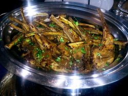 A serving dish filled with cooked lamb chops garnished with chopped herbs.