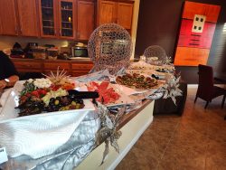 A buffet counter displays assorted meats, cheeses, vegetables, and olives on white platters, decorated with silver ornaments.