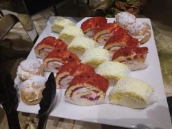 A white plate with assorted desserts, including cream puffs, yellow sponge cakes, and red cake rolls with cream filling.