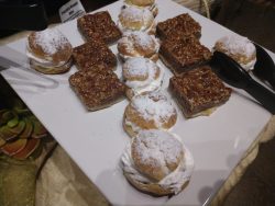 A plate with powdered cream puffs and pecan bars, with serving tongs beside the desserts.