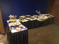 A buffet table with a variety of plated dishes and serving trays arranged against a dark blue wall.
