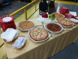 A table with pies, plates, forks, napkins, and holiday decorations set up in an industrial setting.