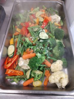 A tray filled with assorted steamed vegetables, including carrots, broccoli, cauliflower, zucchini, and bell peppers.