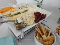 A platter with assorted cheeses, red grapes, and herbs, next to a bowl of crackers and breadsticks.
