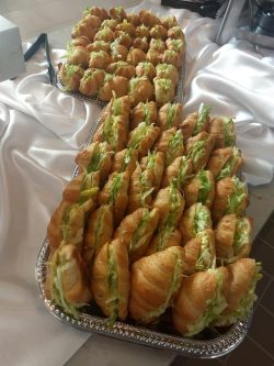 Two trays filled with croissant sandwiches containing lettuce, arranged on a table with a white tablecloth.