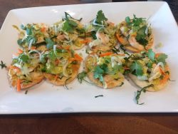 Eight small tostadas topped with shrimp, vegetables, and fresh cilantro are arranged on a white rectangular plate.