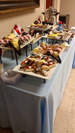 A buffet table with assorted pastries, including cannoli and rolled cakes, displayed on white trays with serving tongs.