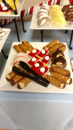 A platter of assorted desserts, including cannoli, jelly squares with cream, and sliced cake rolls, on a white plate.