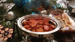 A chafing dish filled with sliced sweet potatoes sits on a festive buffet table with assorted holiday decorations.