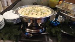 A chafing dish filled with creamy chicken and vegetables, surrounded by festive greenery and blue ornaments.