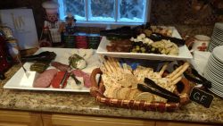 Assorted cheeses, cured meats, olives, artichokes, and gluten-free crackers arranged on platters and a basket on a counter.